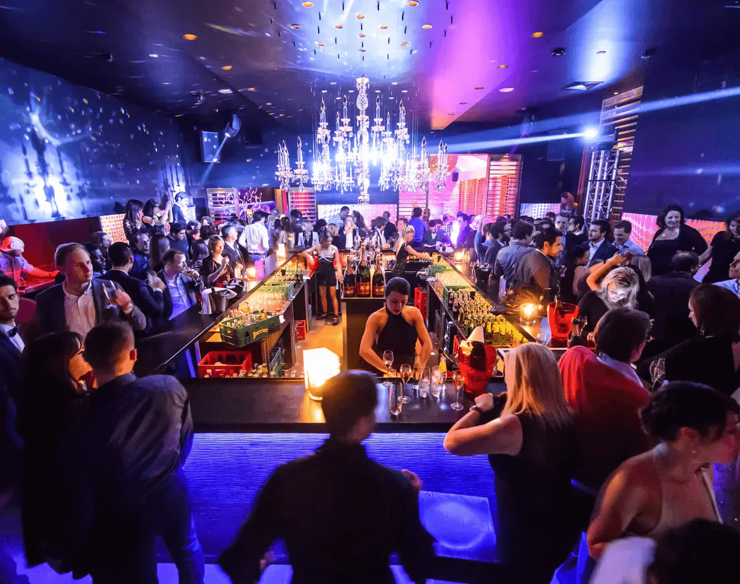 Bar central des Jeux d'Hiver sous un lustre de cristal, entouré d'une foule en tenue de soirée