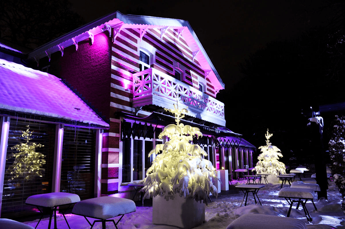 Chalet rayé des Jeux d'Hiver sous la neige, éclairé de violet dans la nuit
